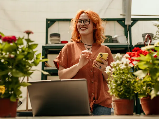 Woman smiling in a garden on her phone